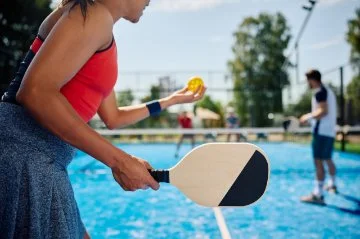 Close up of pickleball player serving the ball during the match on outdoor court.